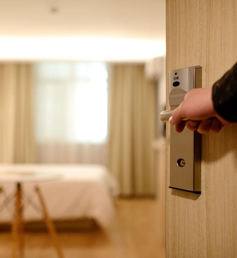 hand opening a door to reveal hotel room interior bathed in warm yellow light perfect for a hotel website blog