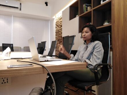 Young woman seated at conference table talking into laptop